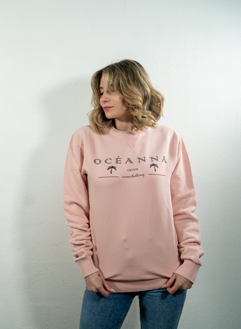 Sudadera rosa sin capucha con el logo de Oceanna Clothing en el pecho.