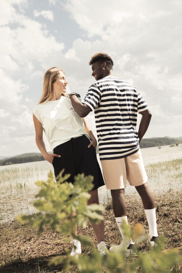 Chica con camiseta sin mangas blanca y pantalón negro corto y chico con camiseta de rayas y pantalón beige, todo de Oceanna Clothing de algodón orgánico.